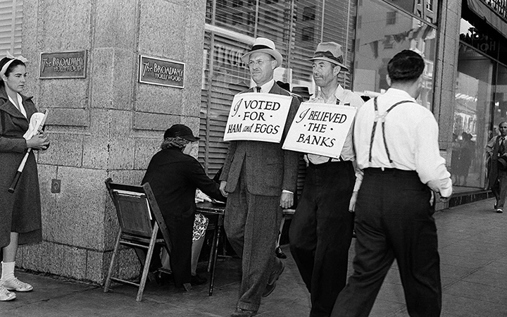 Men wearing sandwich boards reading "I voted for ham and eggs" and "I believed the banks" walk down a Los Angeles street, Oct. 24, 1938.